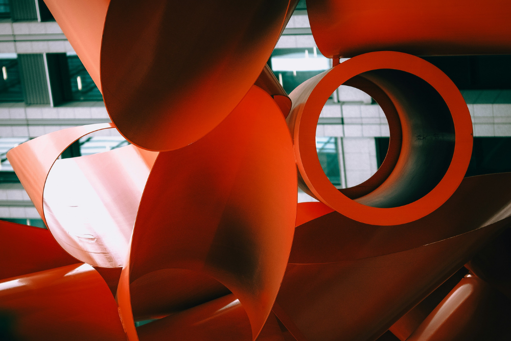 Abstract orange sculpture with curved shapes and blurred building background.